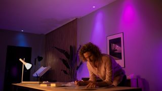 Les lumières DEL intelligentes Philips hue créent une ambiance violette et rose vibrante dans le salon, présentant un éclairage d’ambiance personnalisable pour les soirées cinéma et la détente dans les maisons modernes.