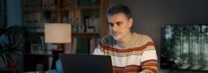 Un homme portant un chandail rayé est assis à son bureau et regarde l’ordinateur portable devant lui