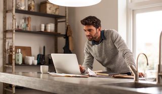 Homme utilisant un ordinateur portable dans des bureaux à domicile bien éclairés avec éclairage de tâche DEL pour une configuration de travail à distance efficace.