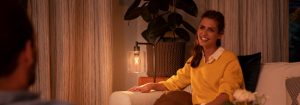 "Ambiance de salon confortable créée par une lampe de table à DEL chaude, illuminant la femme portant un chandail  jaune profitant de la conversation en soirée. »
